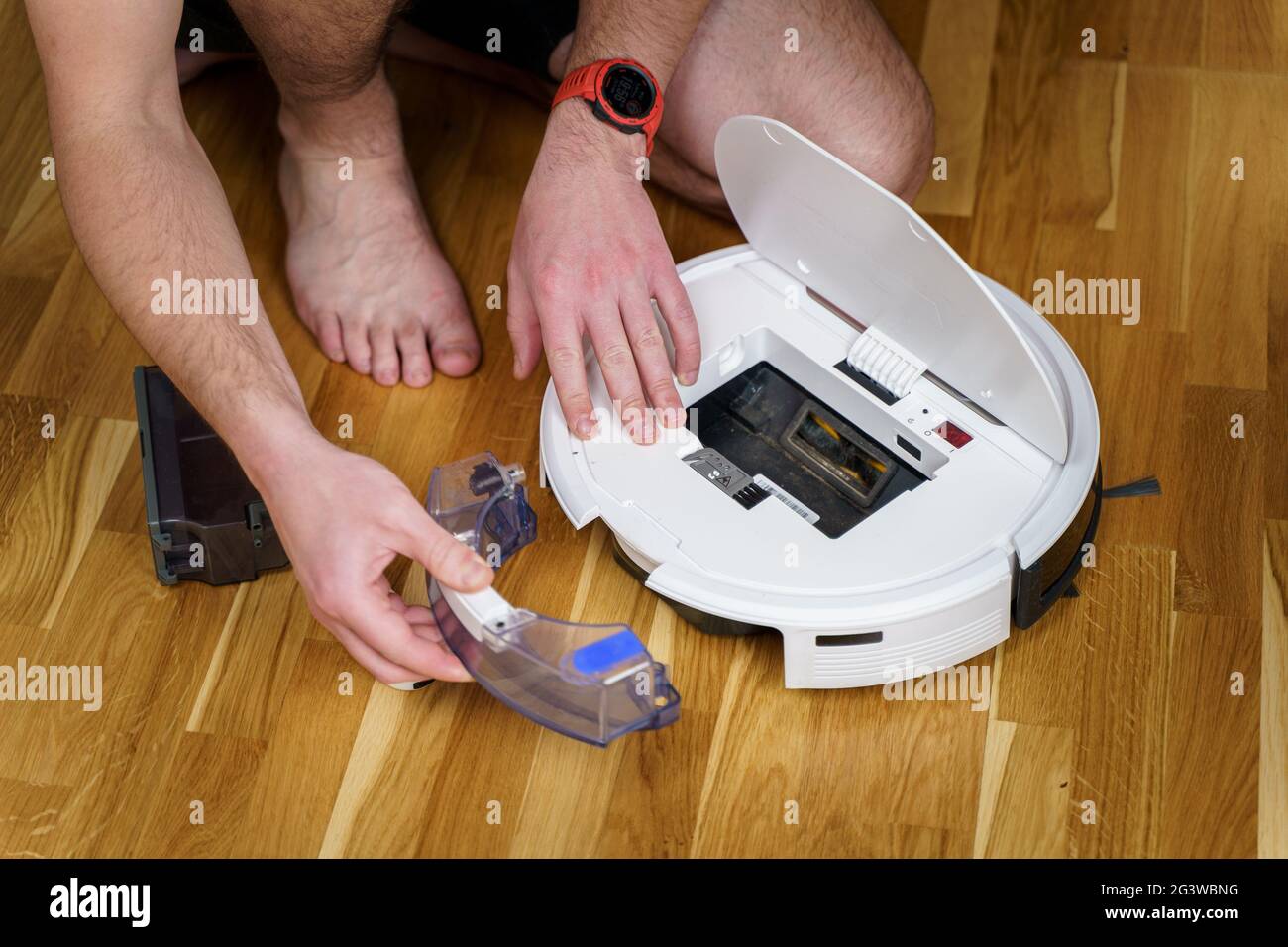 Caucasian young man doing white robot vacuum cleaner maintenance. Autonomous wireless modern vacuum cleaner. Male repairing robo Stock Photo