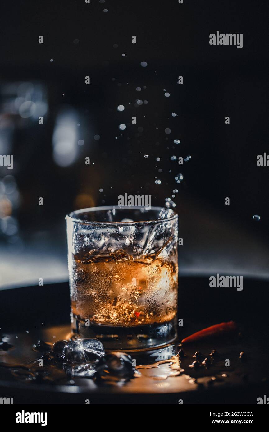Ice cubes fall into a glass - whiskey with ice in a shot. Bar cocktail whiskey and cola. Cold ice in a glass of whiskey. Stock Photo