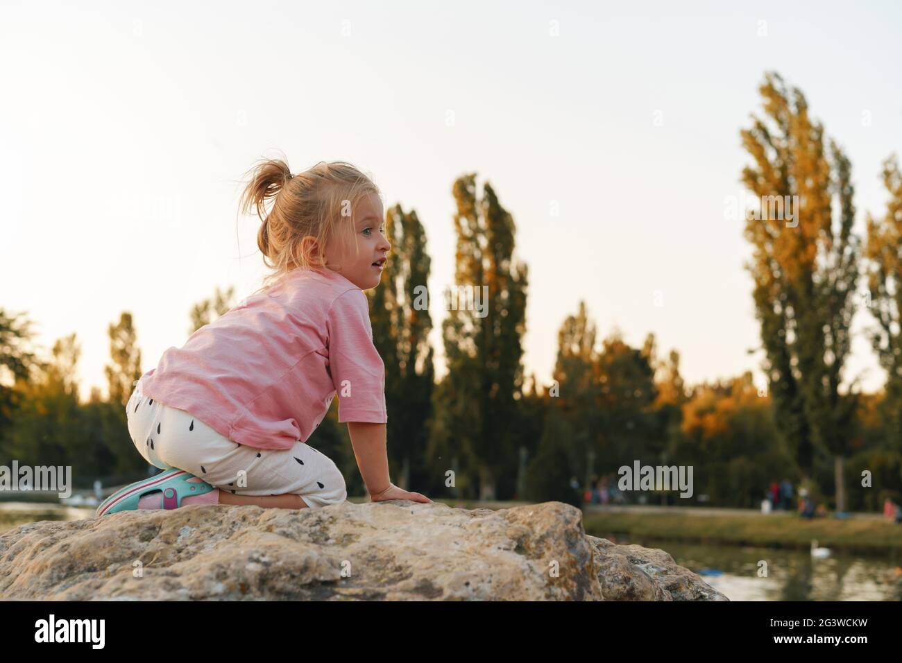 Little girl sitting on a huge stone in park near the lake Stock Photo ...
