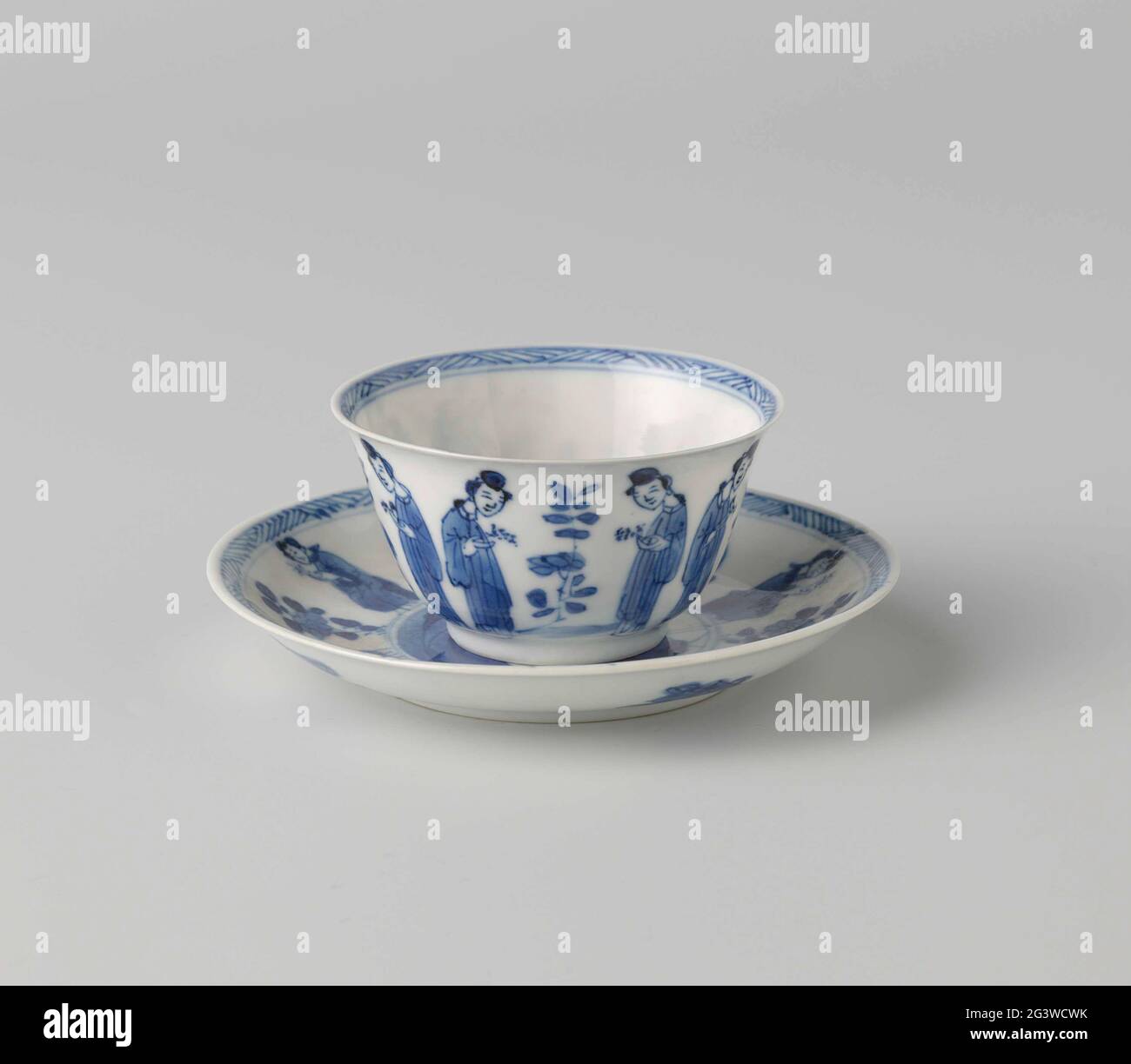 Cup and Saucer with Chinese Ladies and Flower Sprays. Cup and saucer of porcelain, painted in underglaze blue. On the wall of the head, two ladies with a sprig in hand opposite each other with between them in a plant; On the bottom a seated lady in front of a fence at a plant; The inner edge with zig-saw pattern. On the platter of the dish a medallion with a sitting lady at a rock with a plant, to keep the medallion two ladies with a twig in hand at a flower branch; the edge with zig-saw pattern; The back with four valuables (pearl, artemisia leaf, shell, music stone). Dish marked on the under Stock Photo