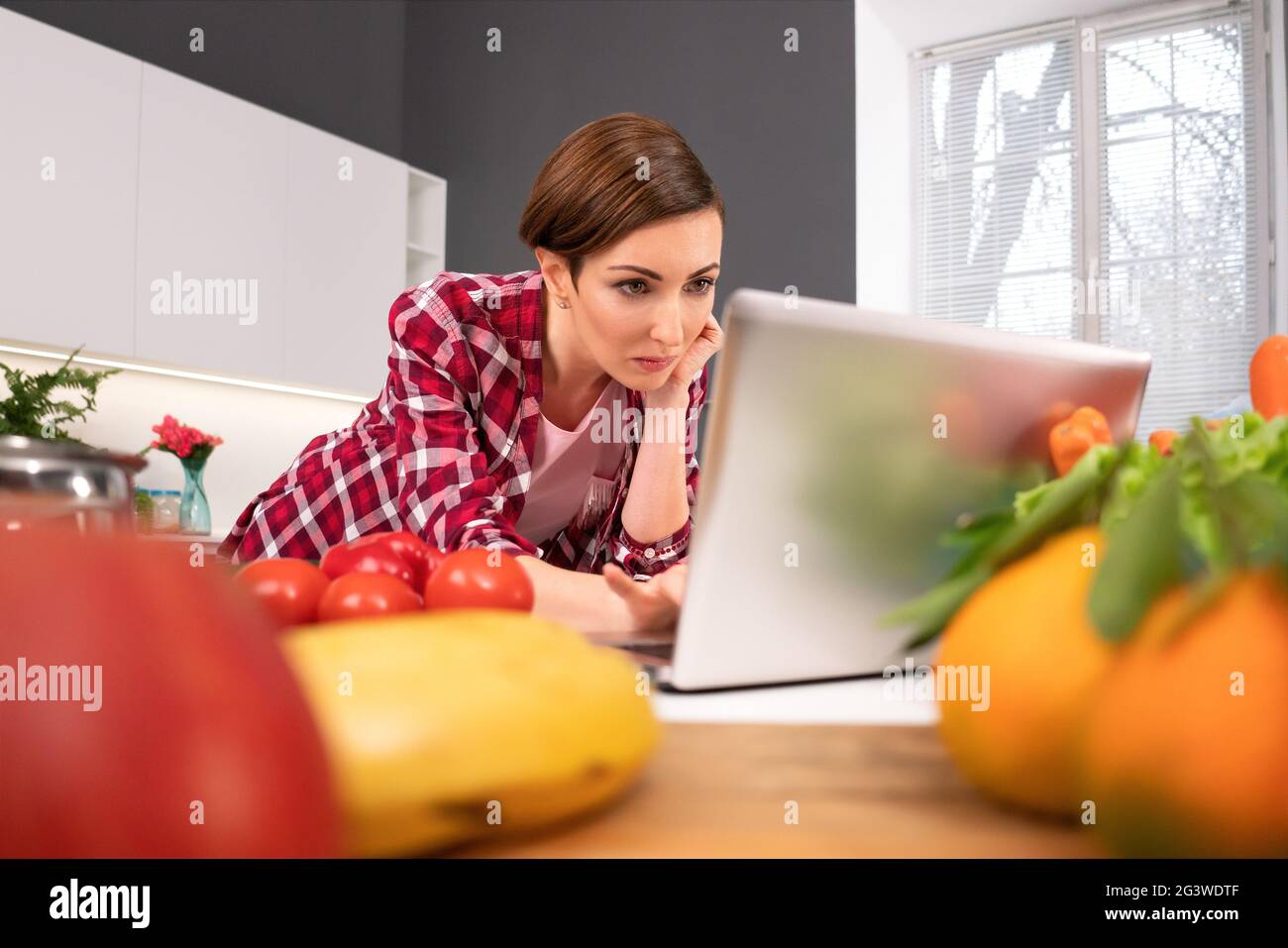 Watching interesting movie using laptop computer housewife forgot about cooking or baking stuck in a monitor. Young woman cookin Stock Photo