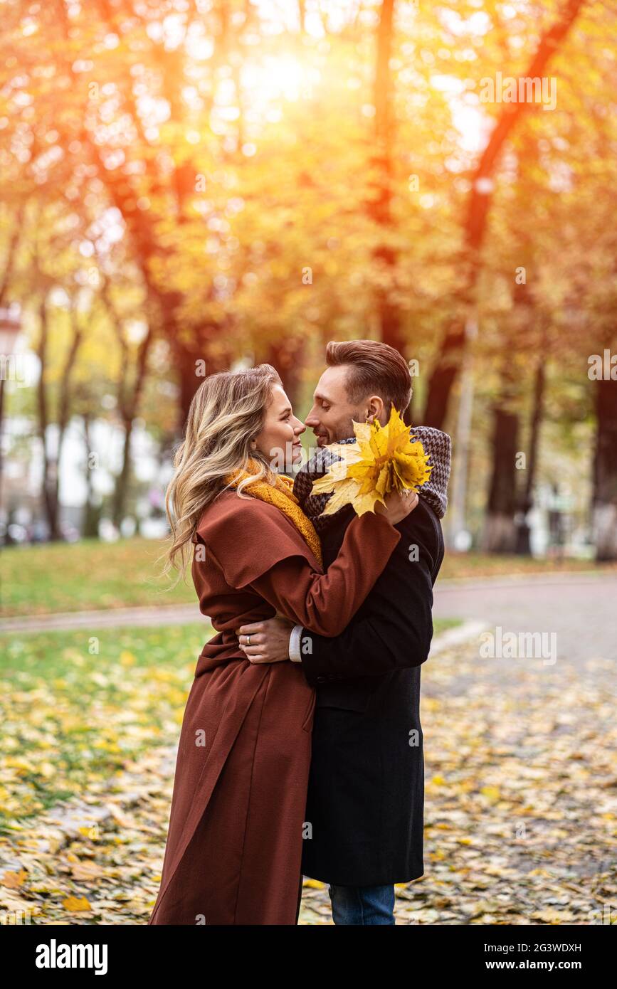 Husband and a wife hugged smile looking at each other in the autumn park. Half-length portrait of a kissing young couple. Outdoo Stock Photo