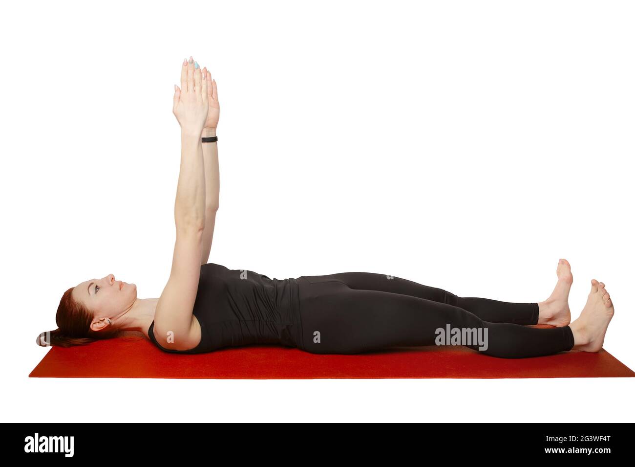 Pilates or yoga. A slender athletic girl lies on her back on a mat with her hands raised in the air. Stock Photo