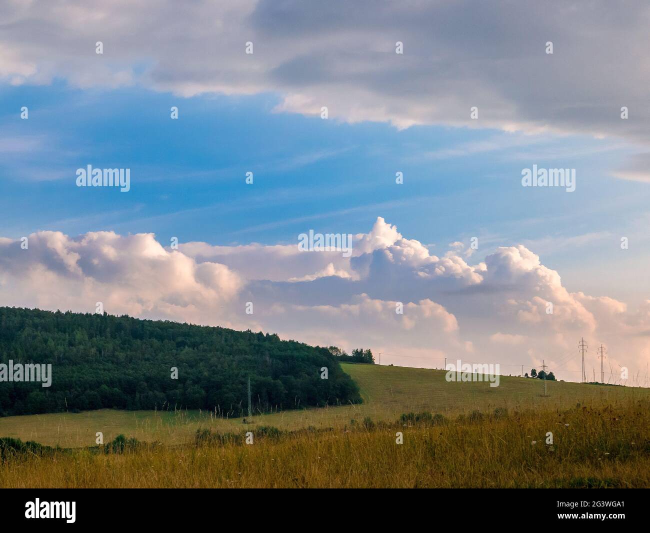 Massive clouds - towering cumulus - forming in the blue sky behind hilly landscape on the horizon Stock Photo