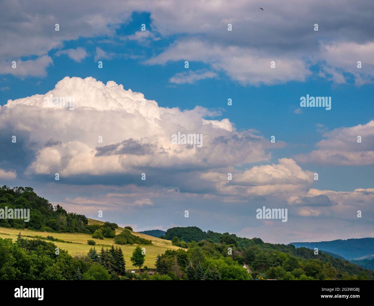 Massive rain clouds forming in the blue sky over hilly landscape Stock Photo