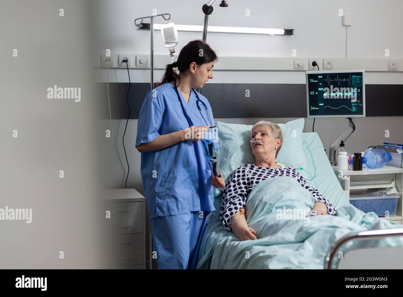 Nurse discussing with elderly patient laying in hospital bed during