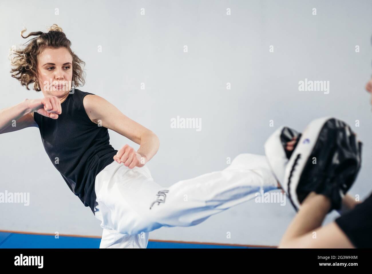 Female martial arts fighter practicing with trainer, punching taekwondo kick pad exercise kicking. Training of kickboxer woman s Stock Photo