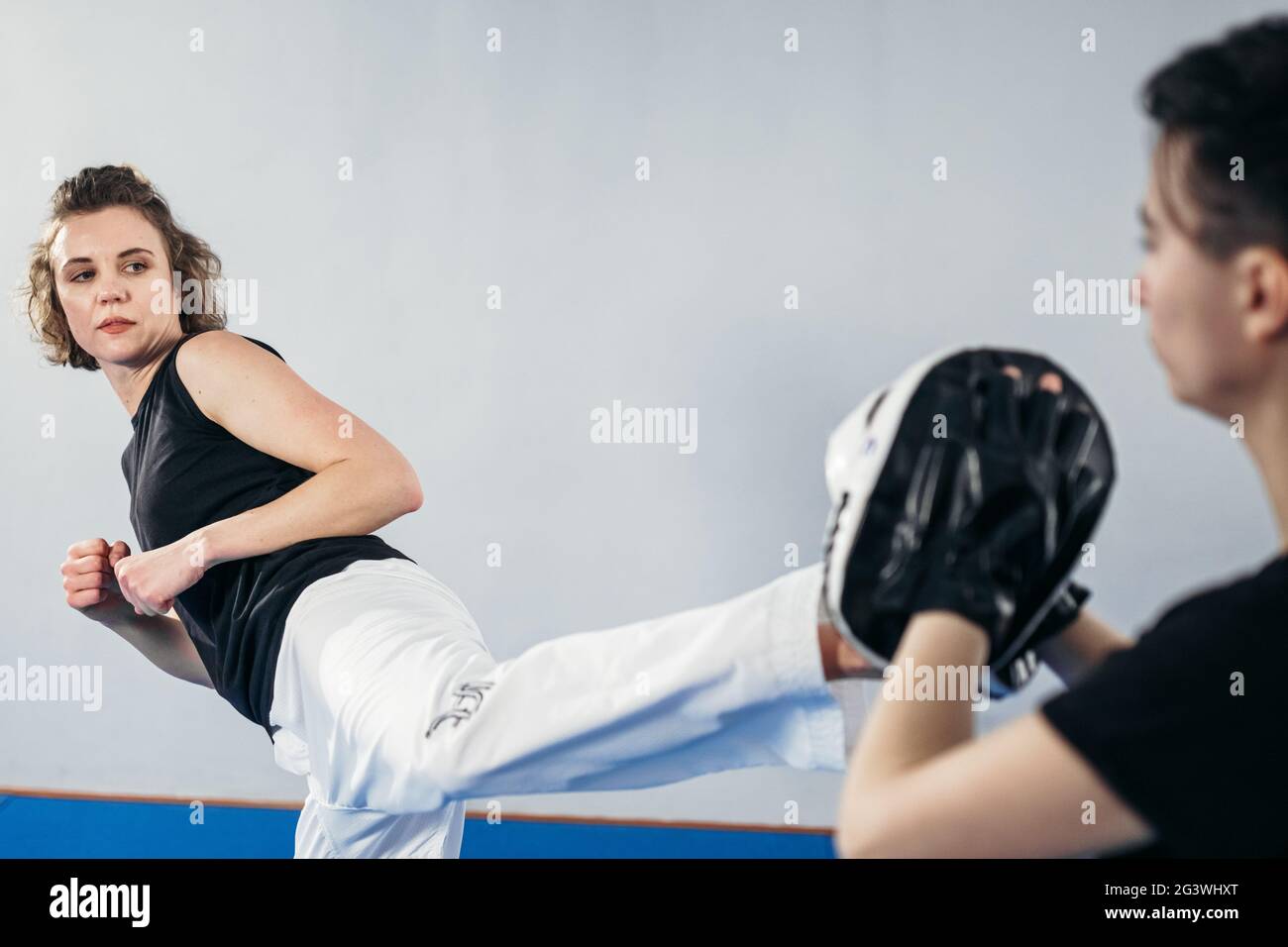 Close-up of barefoot woman leg practicing kicking with taekwondo coach who holds boxing paw. Concentrated active female kicking Stock Photo