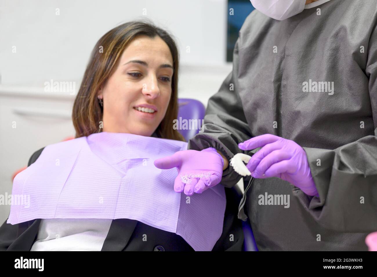 Dentist showing to woman patient an orthodontic silicone trainer. Mobile orthodontic appliance