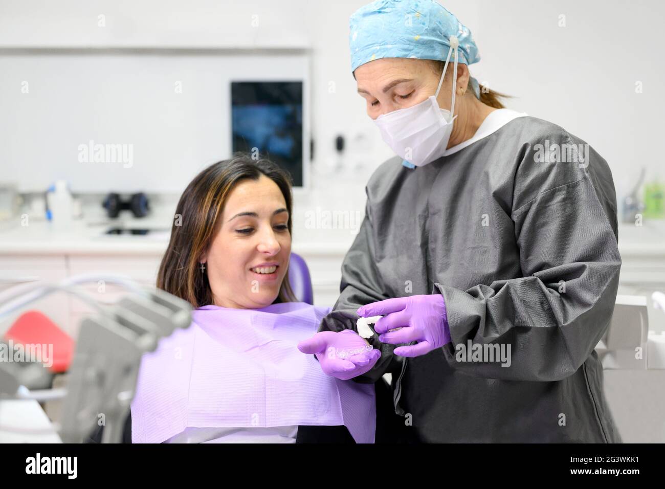 Dentist showing to woman patient an orthodontic silicone trainer. Mobile orthodontic appliance