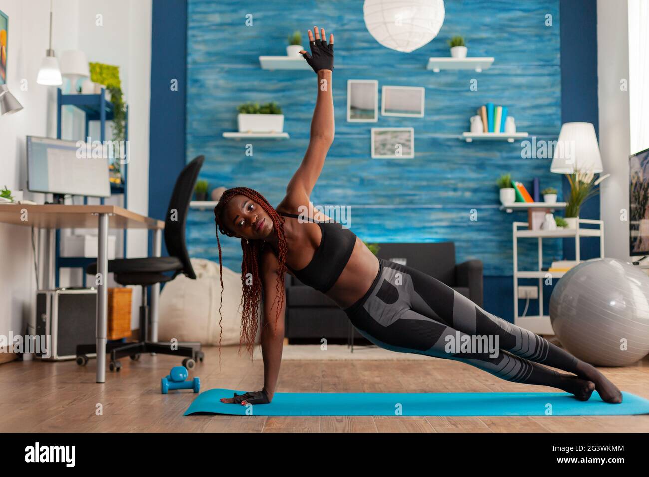 Fit athletic black woman standing in side plank on yoga mat in home living room, doing strenght exercises, training for healthy lifestyle. Full lenght of african american working out. Stock Photo