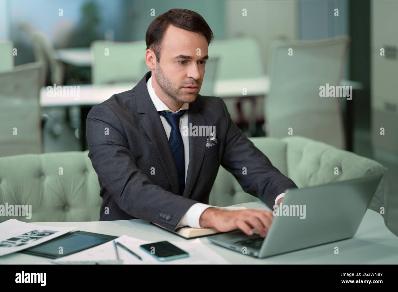 Freelancer sitting in front laptop in bright coworking space. Handsome man in business suit working on laptop, freelancer job in Stock Photo