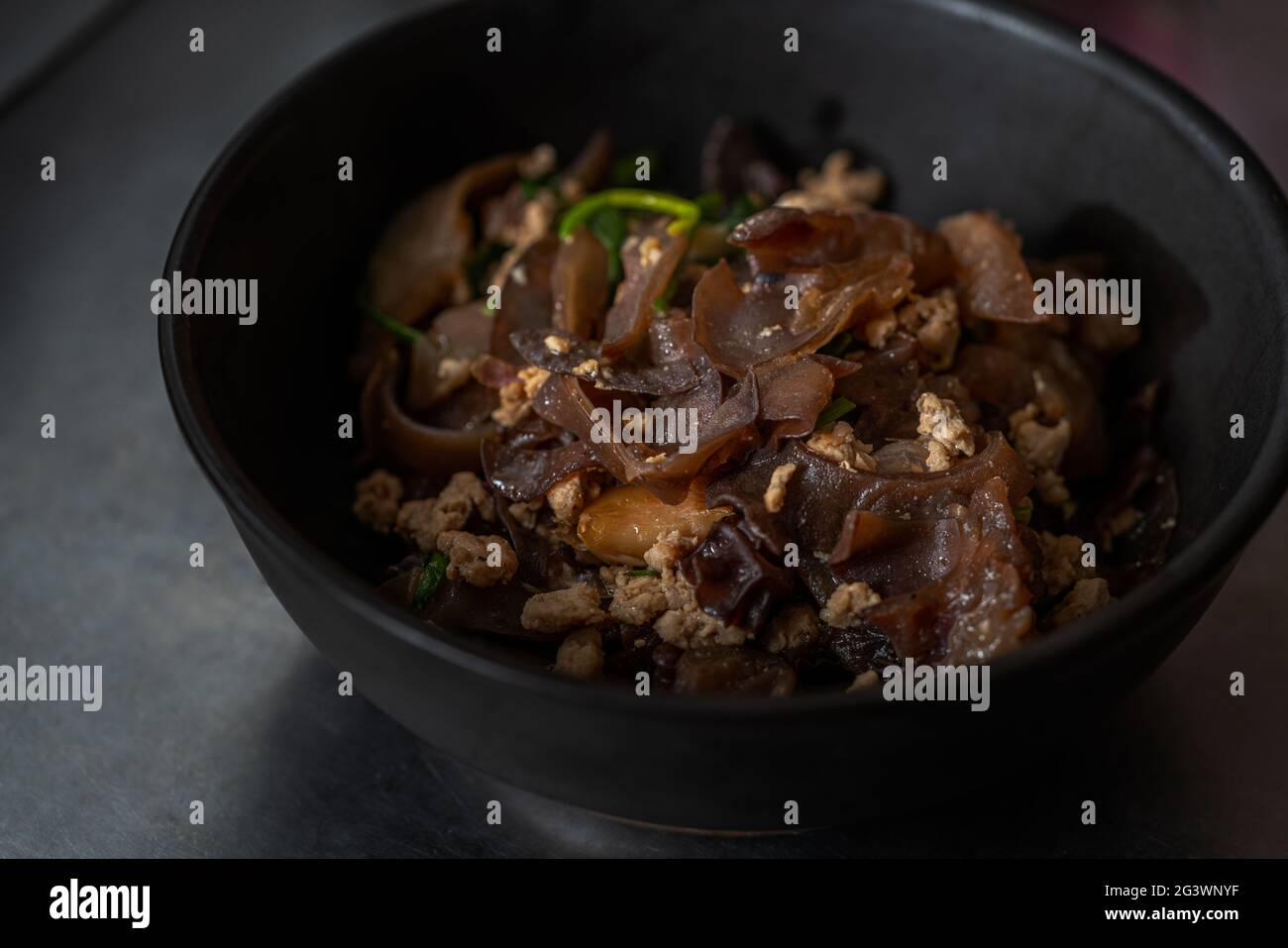 Stir-fried Wood ear and minced pork with scallion, garlic, and soy sauce. Homemade healthy Asian food. Food in a beautiful matt black bowl, close up t Stock Photo