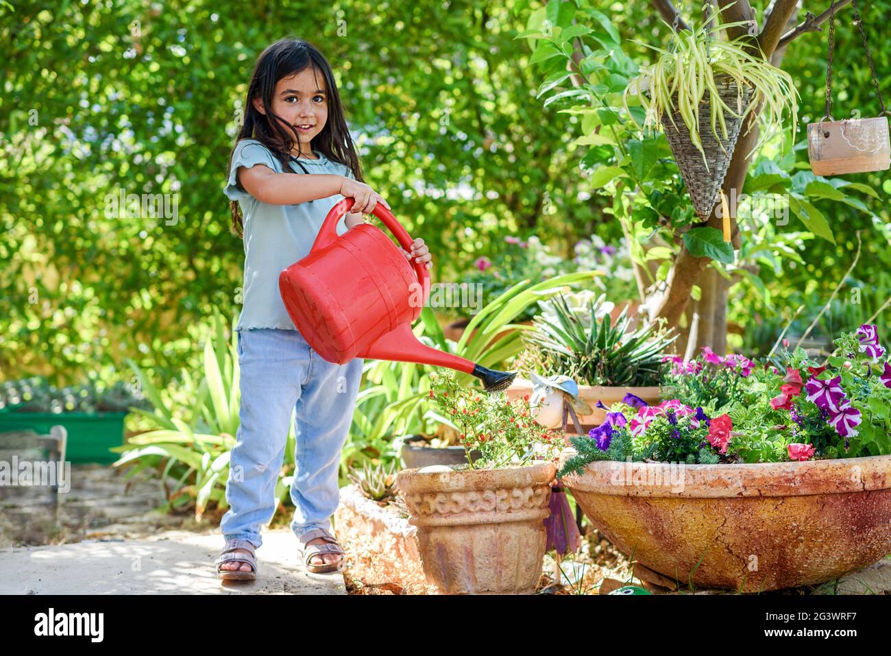 Little girl watering plant in sustainable clay flower pots in a garden