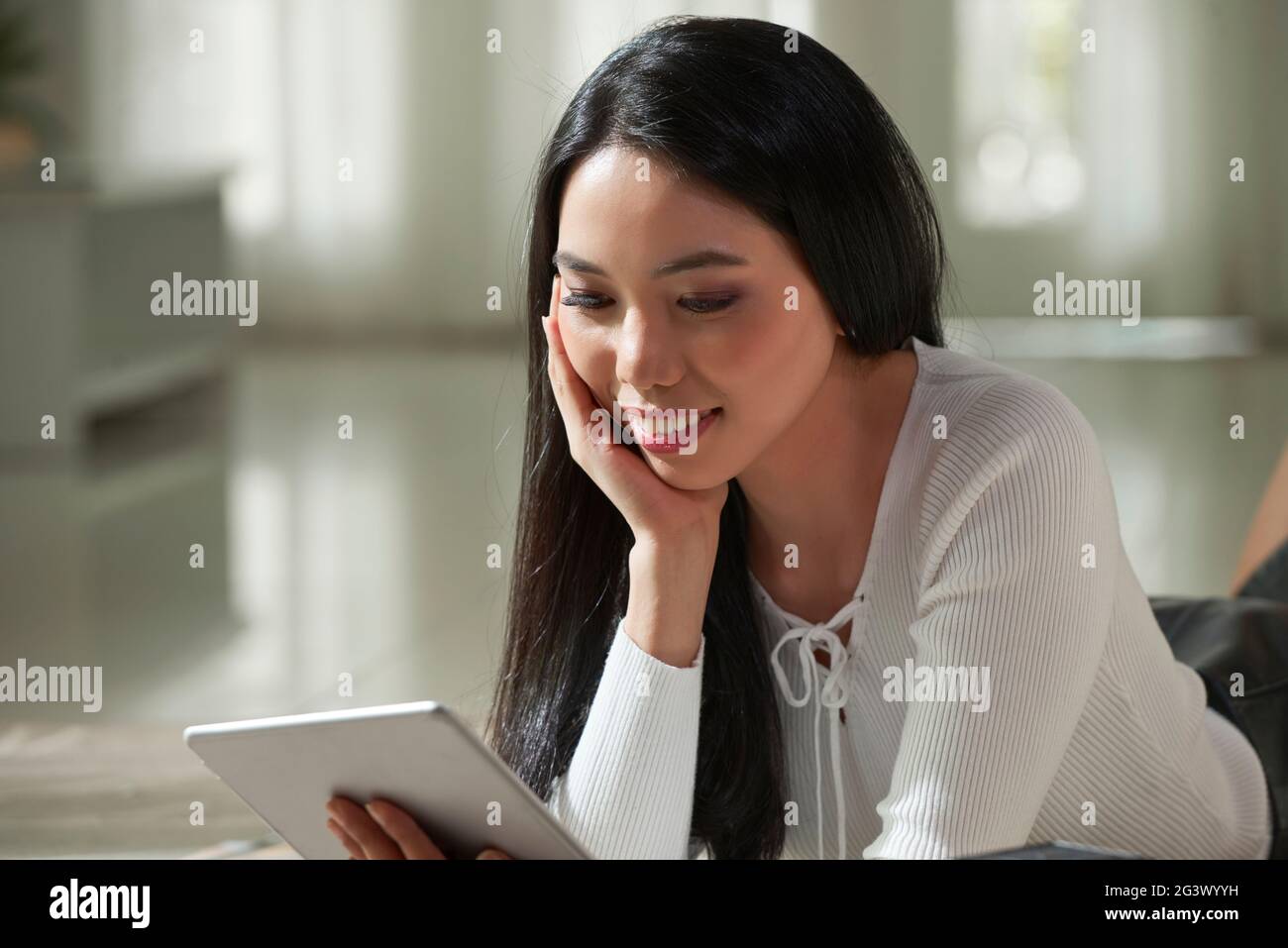 Happy young Vietnamese woman with black hair lying on floor and leaning  head on hand while watching video on tablet Stock Photo - Alamy