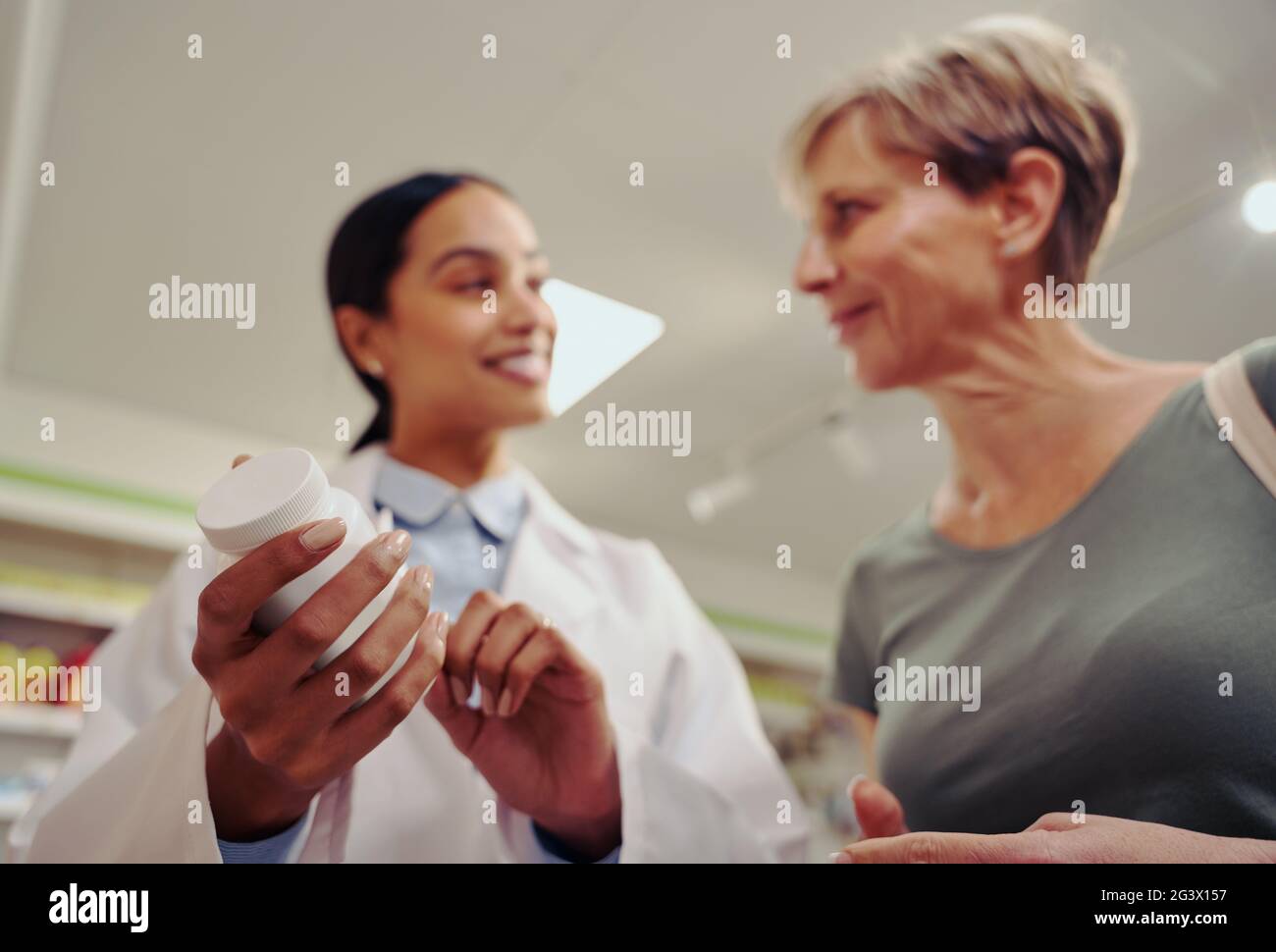 Closeup of young pharmacist hand holding and checking medicine dosage and ingredients with expiry date standing near shelf in chemist shop with senior Stock Photo