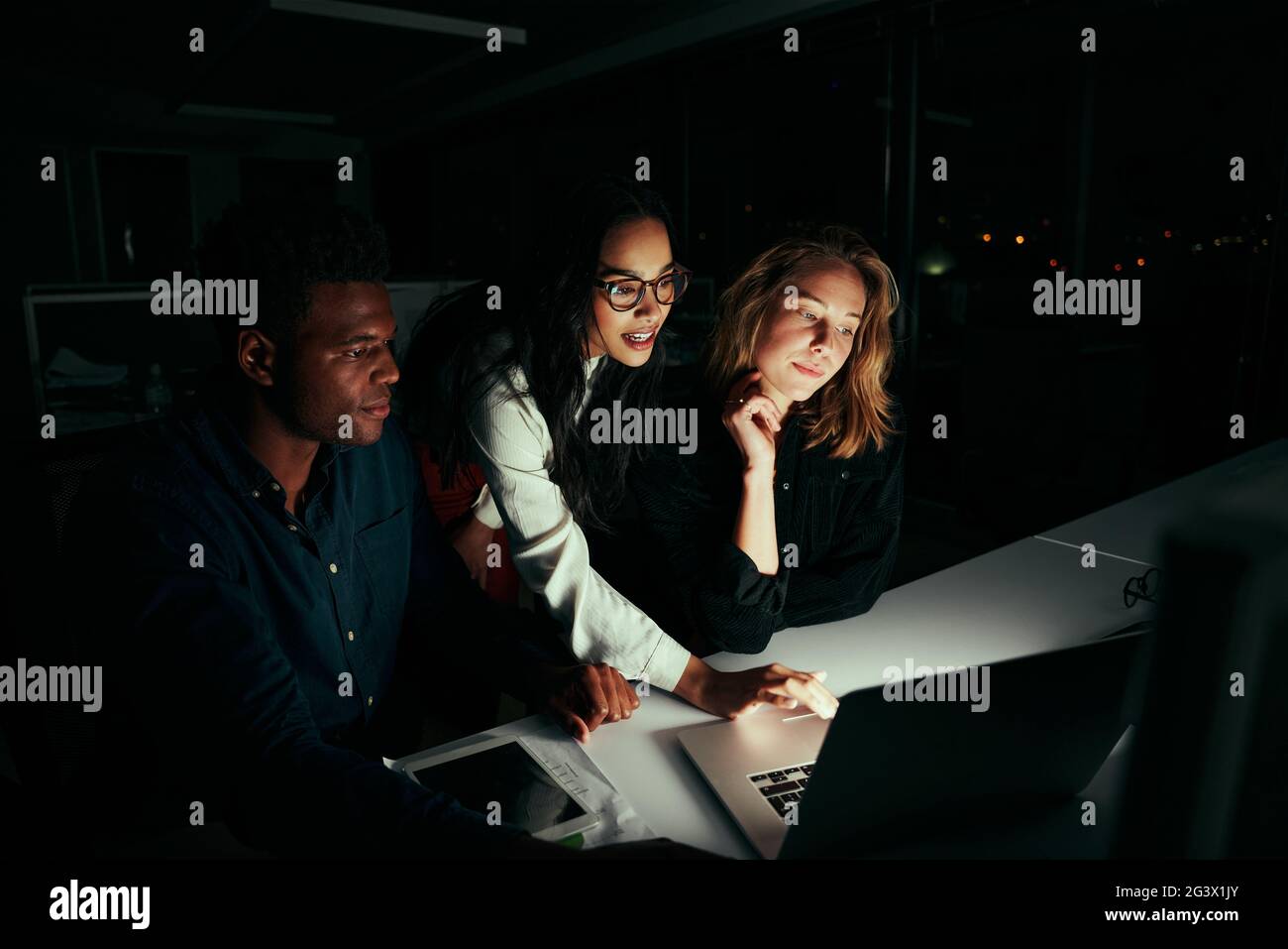 Group of diverse business people working overtime in dark office using laptop Stock Photo