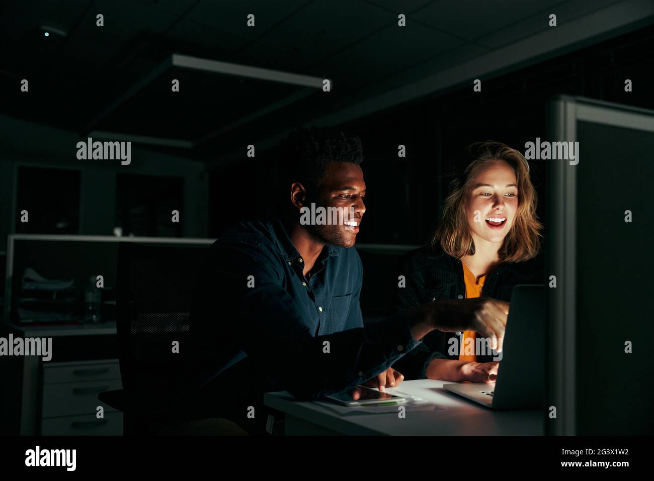 Happy businessman and businesswoman working on laptop overtime in night time Stock Photo