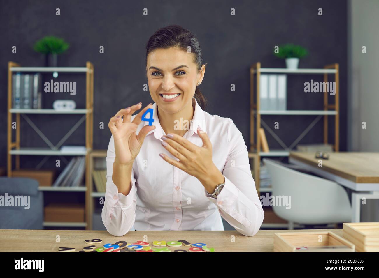 Young smiling woman shows the number 4. A young woman in a white blouse of European appearance Stock Photo