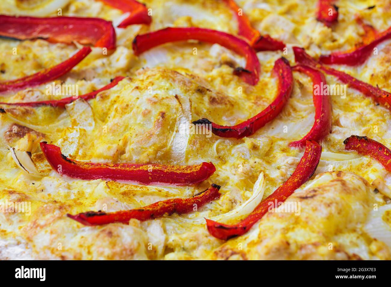 Close-up of pizza topped with red pepper, onion and yellow curry sauce. Macro shot of delicious products. Stock Photo