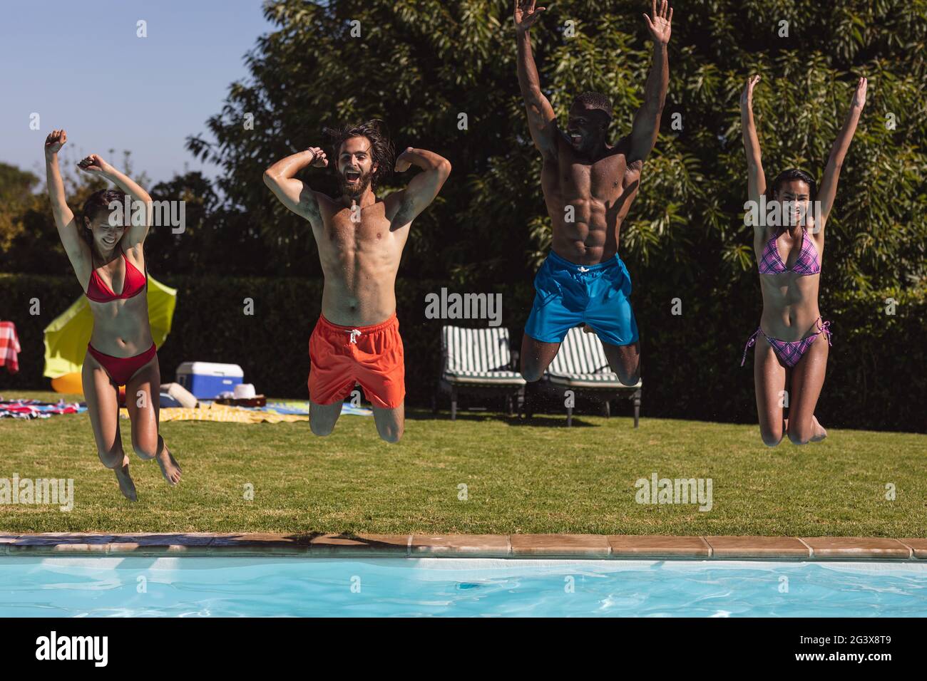 Diverse group of friends having fun and jumping into water at a pool ...