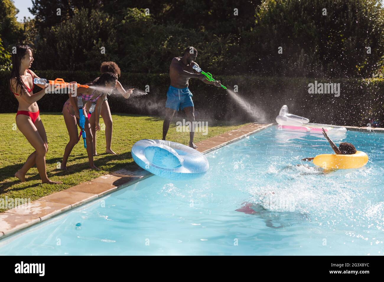 Diverse group of friends having fun playing with water guns at a pool ...