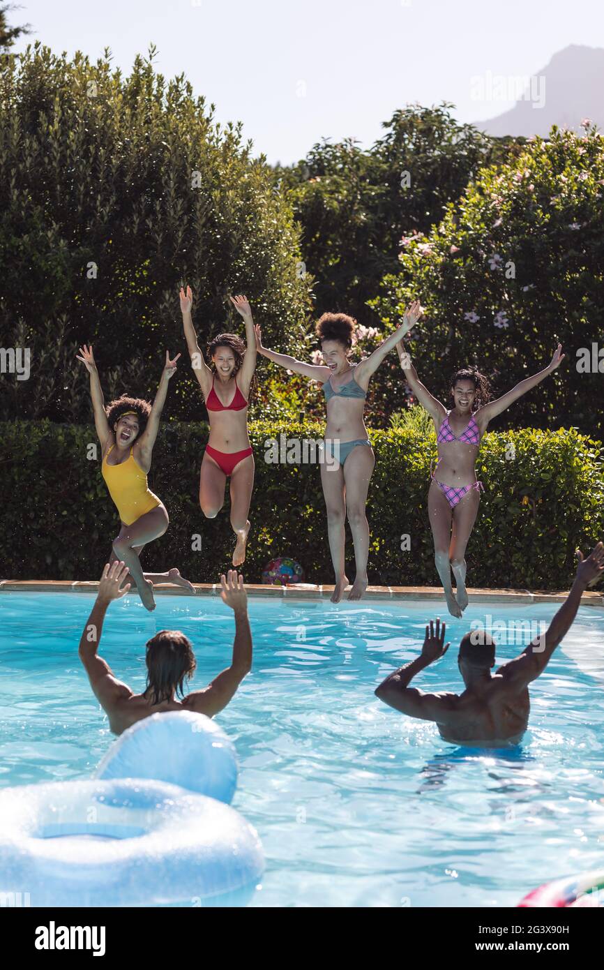 Diverse group of female friends jumping into water at a pool party ...