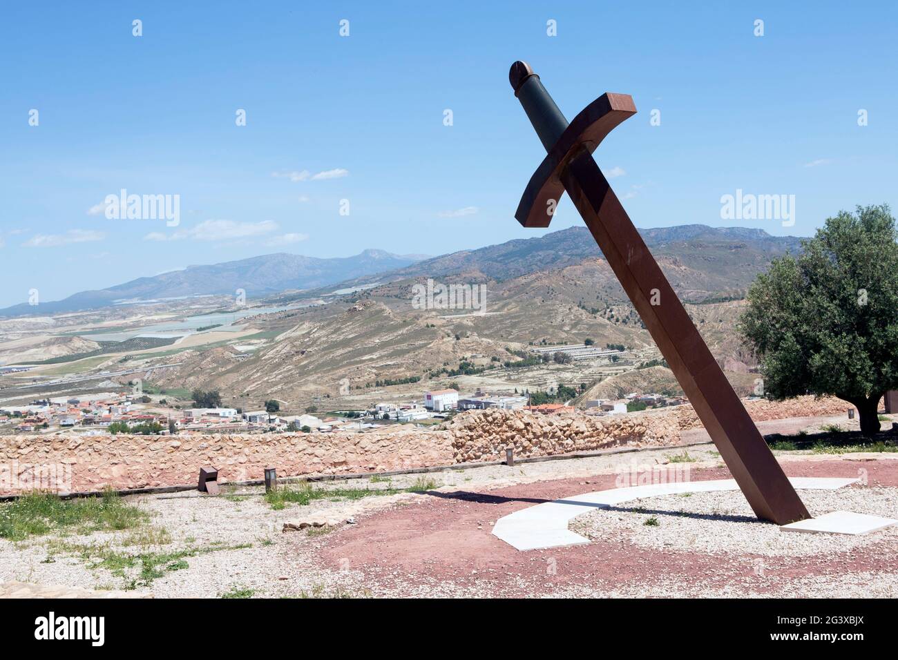Giant iron sword stuck in the ground to give the time with the shadow (sundial) located in the medieval castle of Lorca, Murcia, Spain. and with a fan Stock Photo