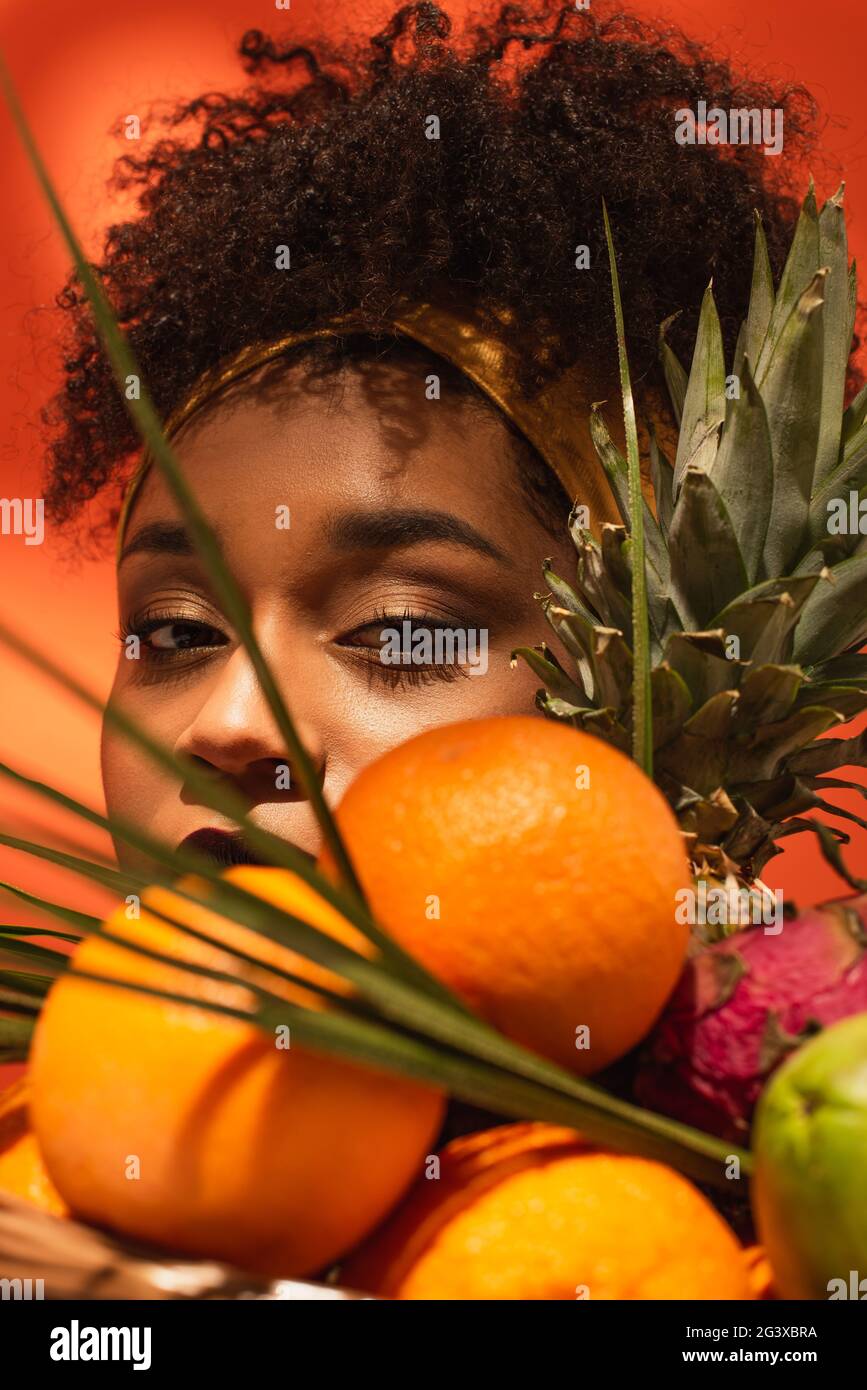 young african american woman hiding face behind fruits with palm leaves ...