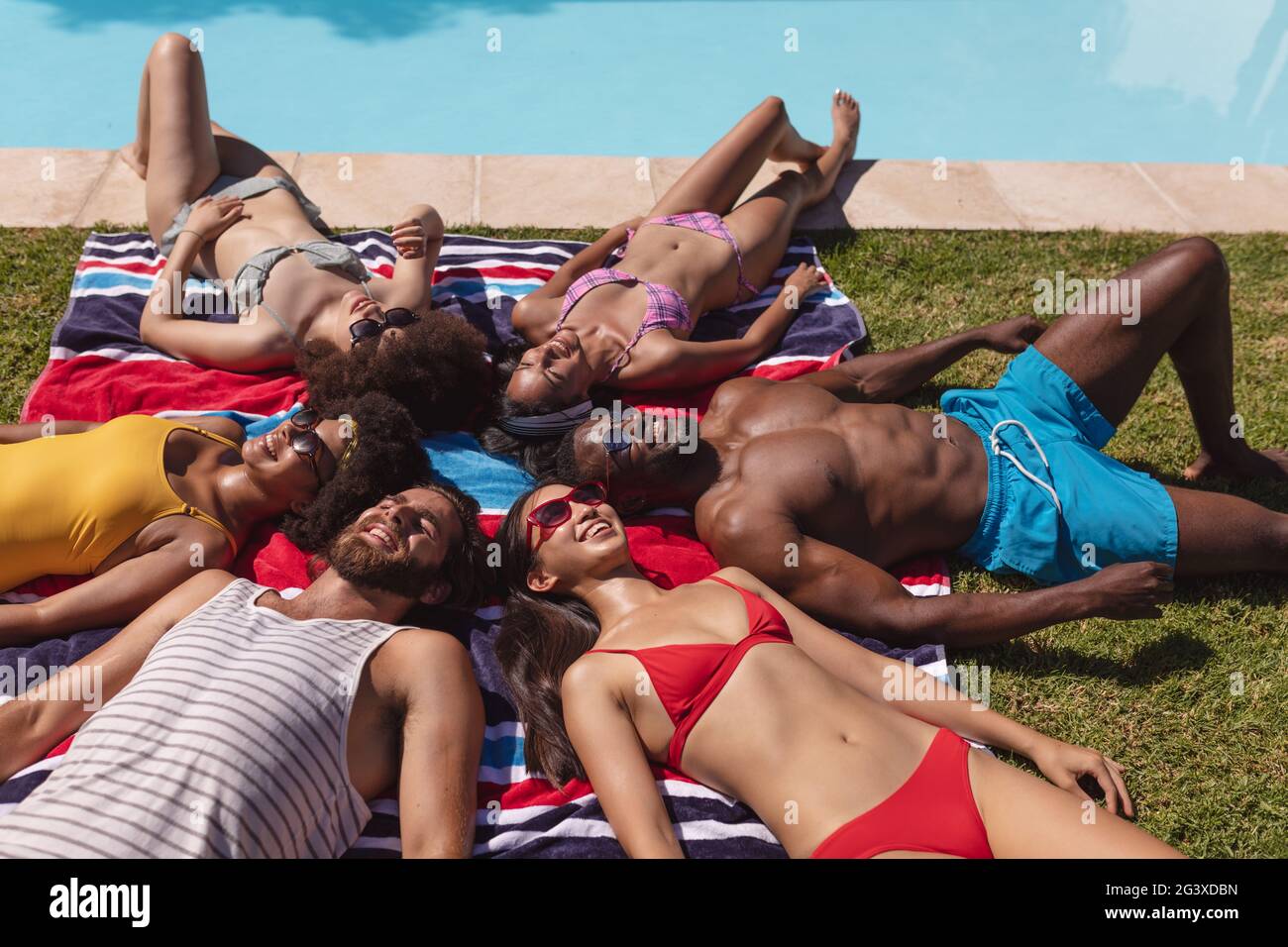 diverse-group-of-friends-sunbathing-together-by-pool-on-a-sunny-day