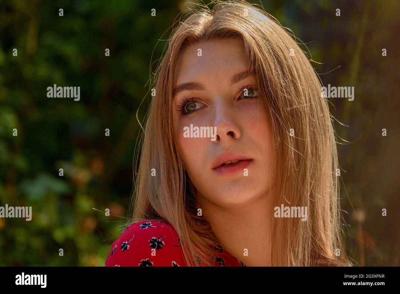 A girl in a red dress with long hair on a background of greenery in ...