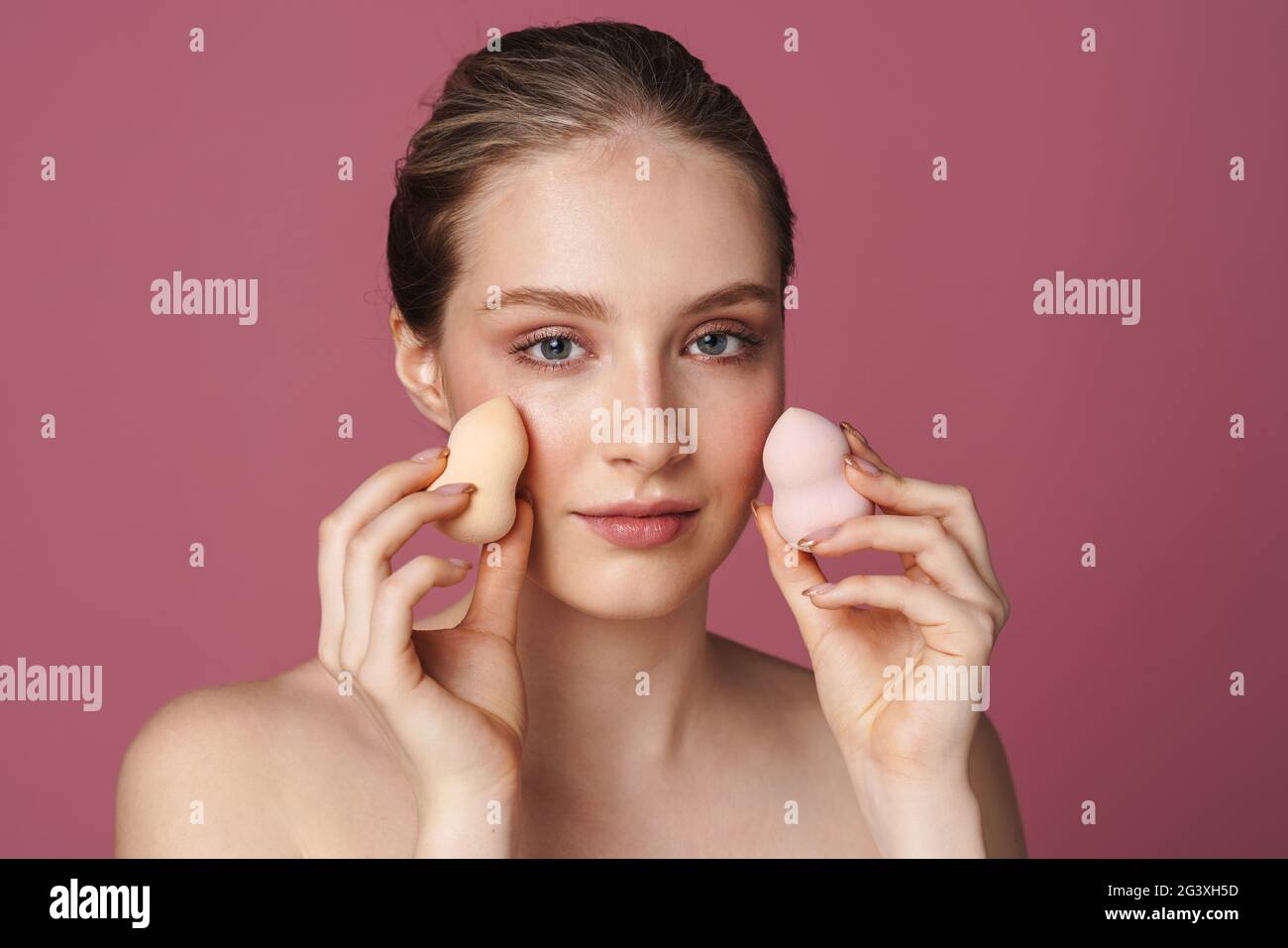 Beautiful young woman applying makeup using beauty blender sponge isolated over pink background Stock Photo