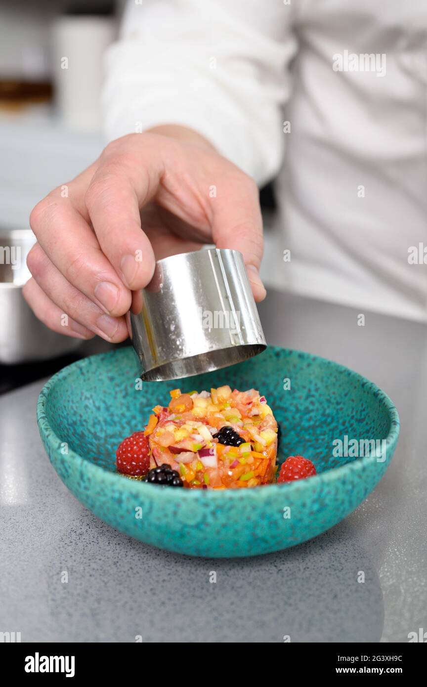 A chef prepares delicious vegetables tartare and finishes the preparation with a touch of class. Concept of: chef, kitchen, rest Stock Photo
