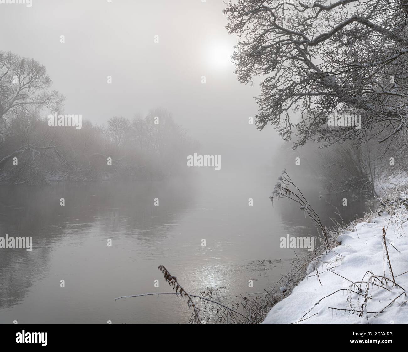 Sun breaking through the mist over the Teviot River in winter snow in the Scottish Borders Stock Photo