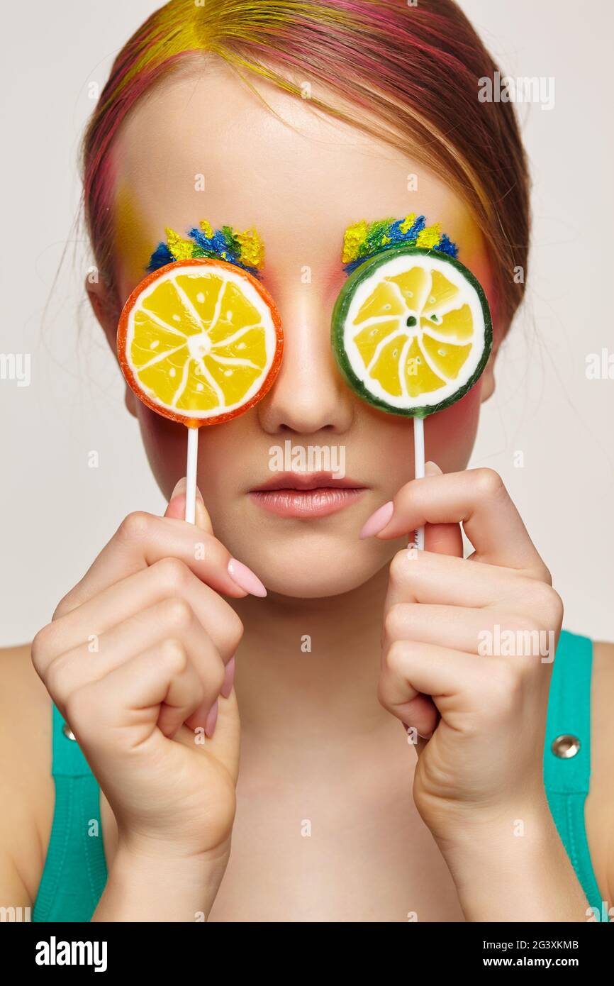 Teenager girl with unusual face art make-up . Child with lollipops in hands closing eyes. Stock Photo