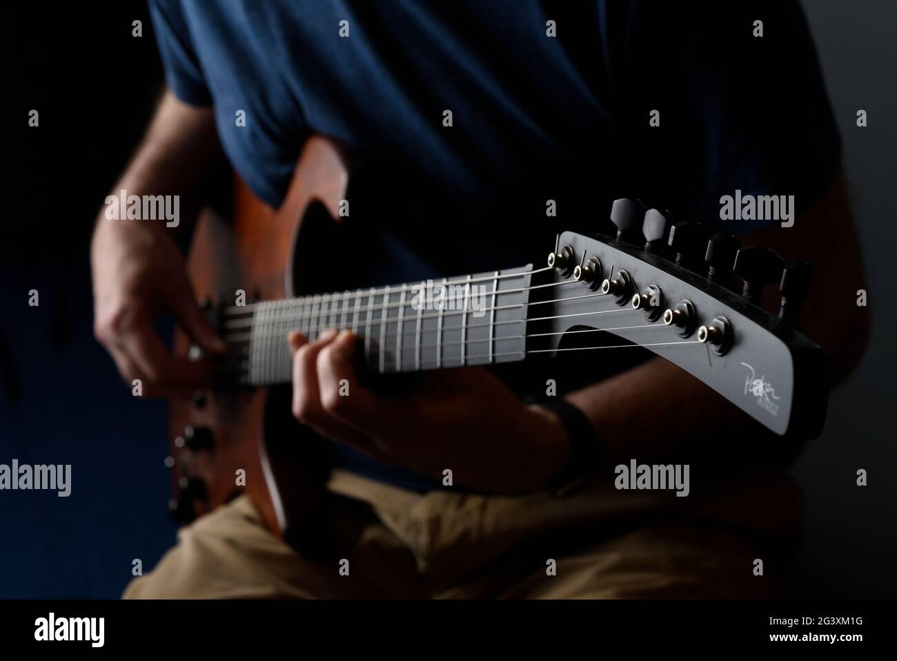 Close up of a man playing a guitar. Dark background, blue shirt and selective focus. Stock Photo