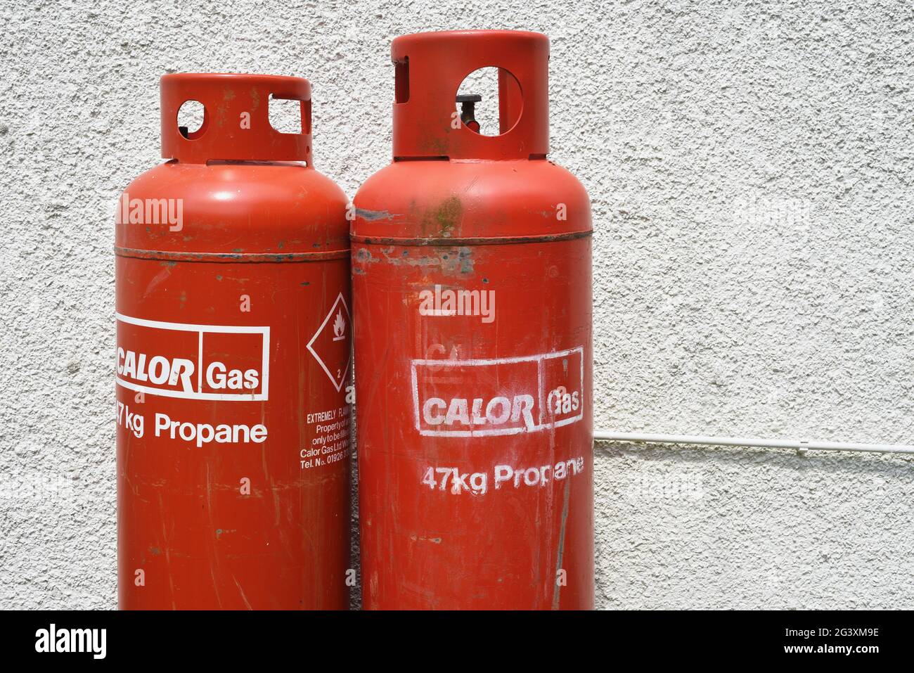 Two large red 47kg Calor gas canisters / propane against a white wall Stock Photo