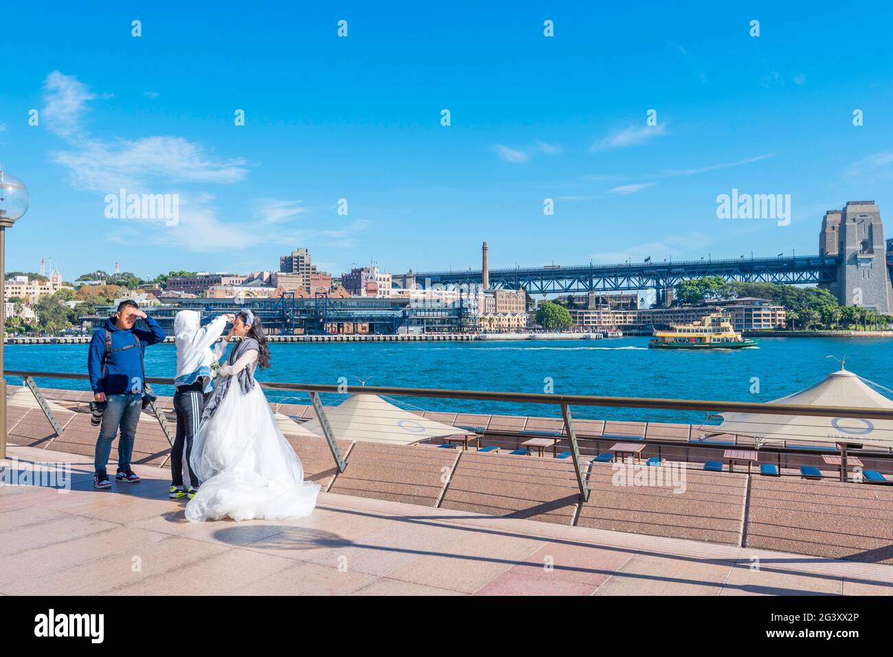 A bride at the Sydney Opera House and Sydney Harbour in Australia gets her makeup adjusted while a photographer patiently waits Stock Photo