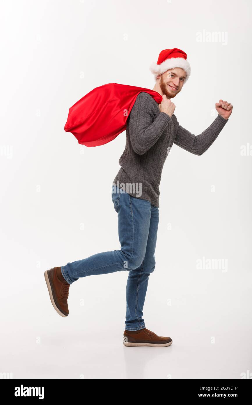 Christmas concept - Young confident beard man running and holding red big santa bag with a lot of present inside. Stock Photo