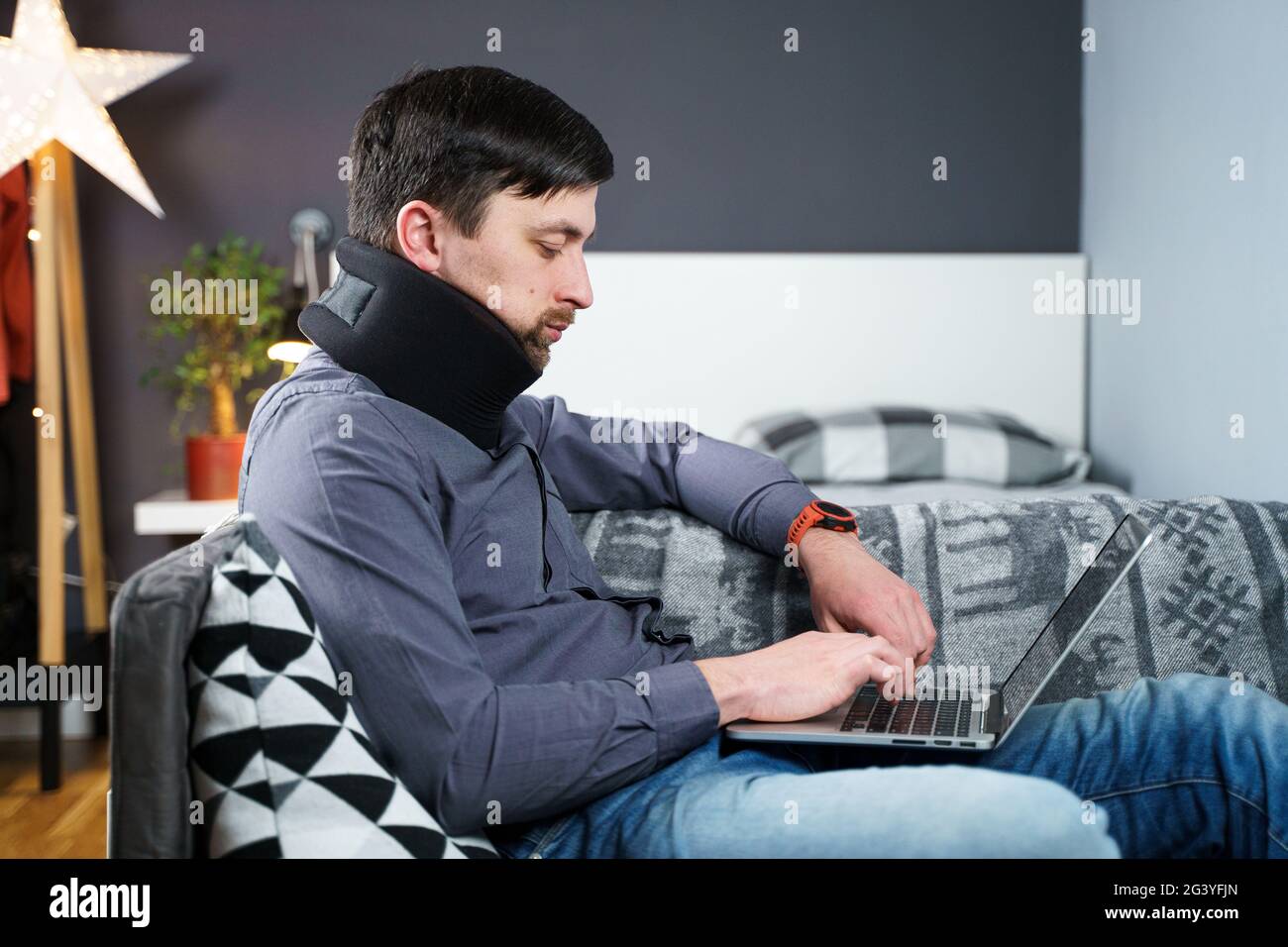Man employee after accident working at home behind laptop and feels pain in neck, uses black neck collar support. Male with neck Stock Photo