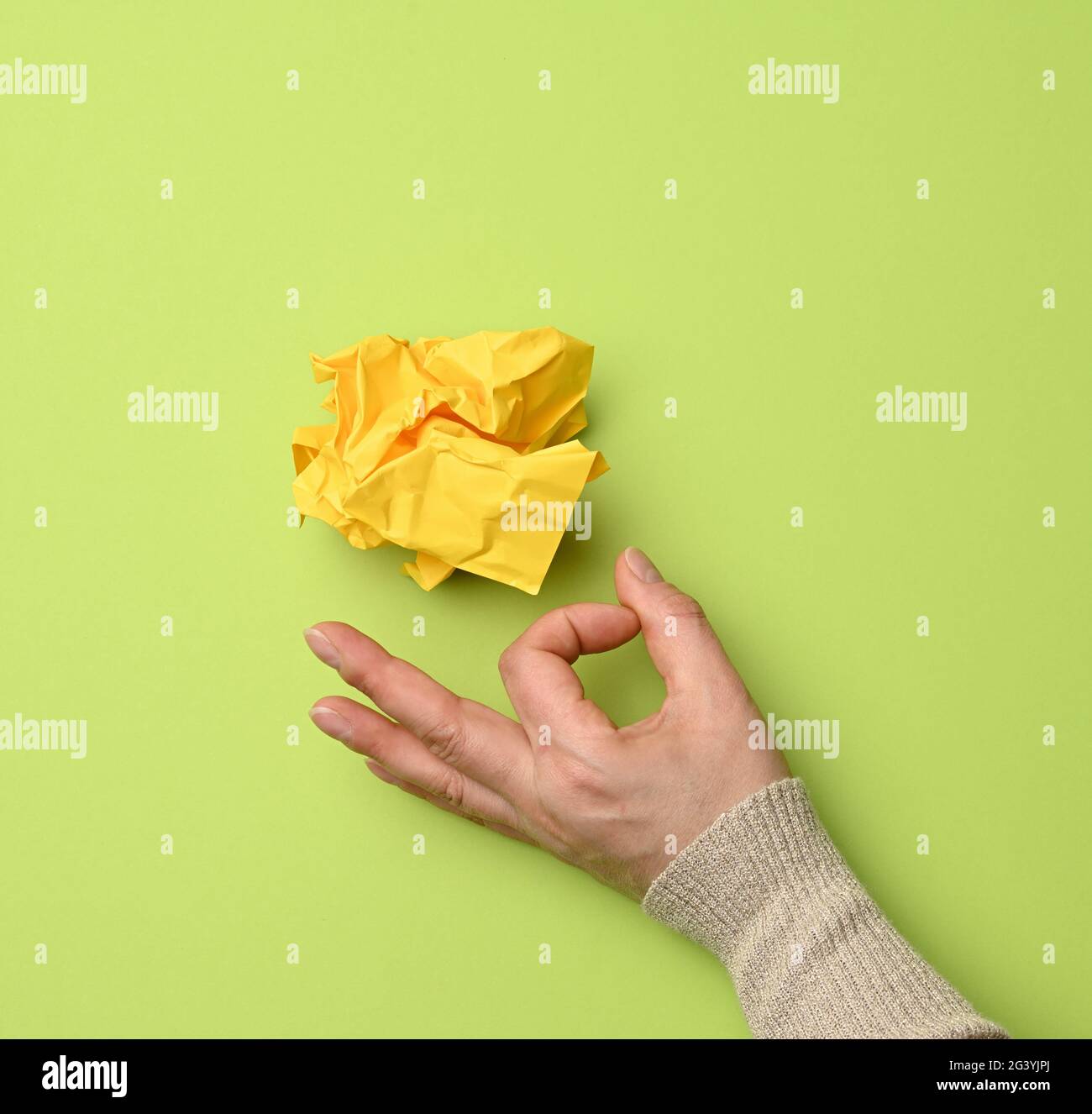 Yellow crumpled ball of paper and female hand on a green background