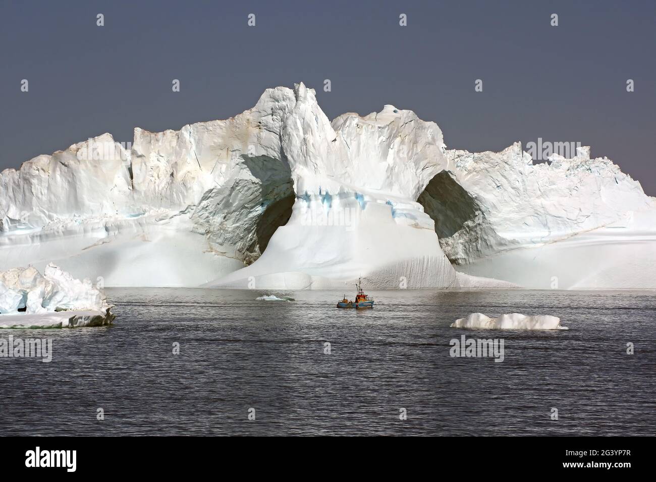 Small fishing vessel in front of icebergs, Ilulissat Stock Photo