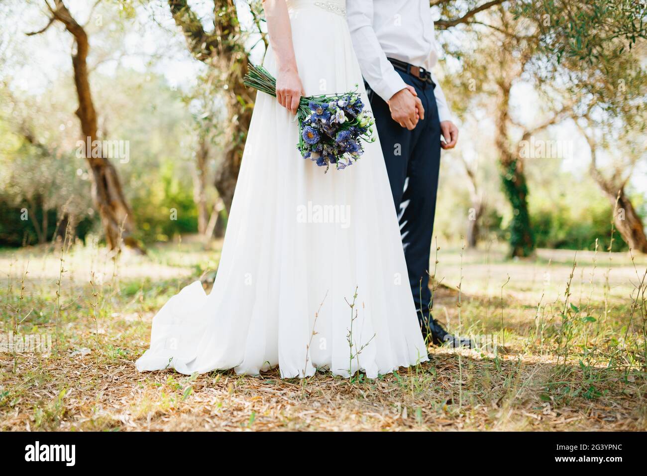 Bride with a bouquet of blue flowers and the groom stand side by side ...