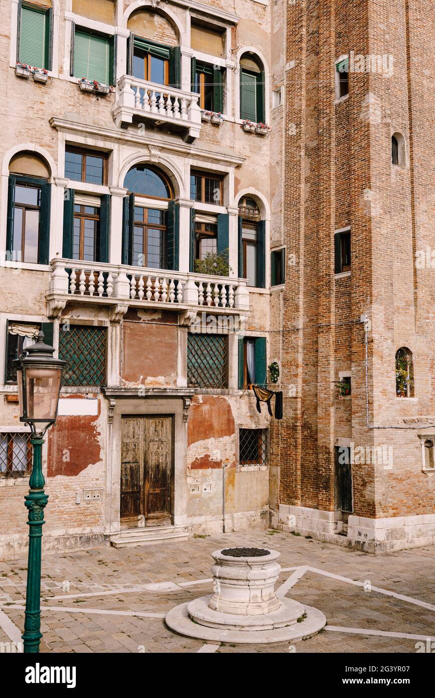 Close-ups of building facades in Venice, Italy. An old street well in the square in front of a brick house. There are many Venet Stock Photo