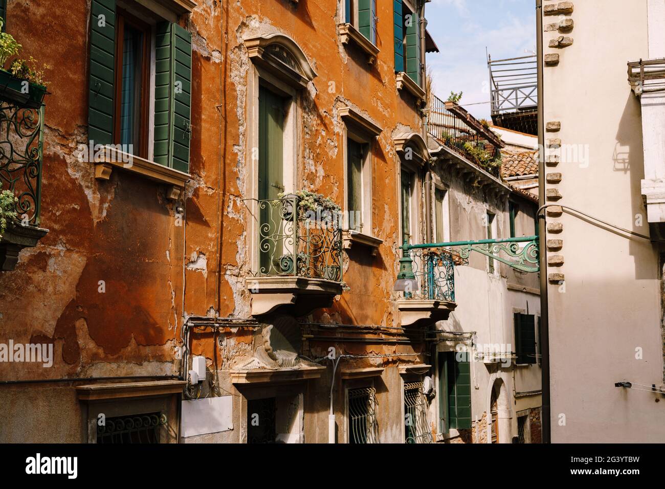 Close-ups of building facades in Venice, Italy. Green wooden door at bottom of brick house. Balcony with a forged fence. An old Stock Photo
