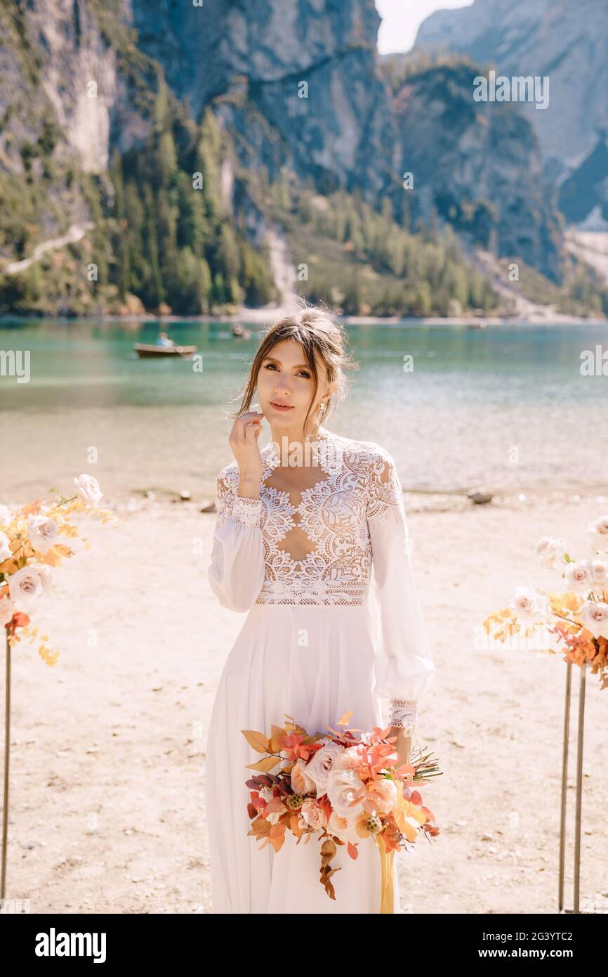 Beautiful bride in a white dress with sleeves and lace, with a yellow autumn bouquet on background of the arch for ceremony, at Stock Photo