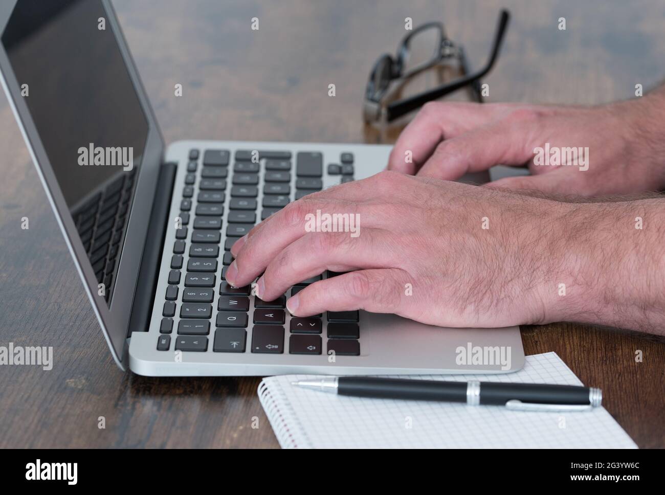 side view close-up of person working on laptop computer at wooden desk Stock Photo