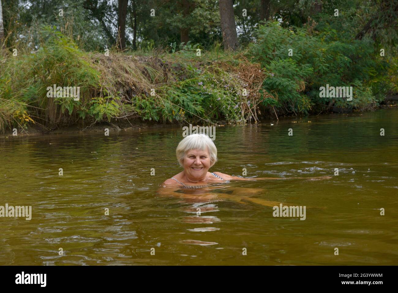 Close-up portrait of smiling elderly woman that is posing in the river water in cloudy autumn day. Stock Photo