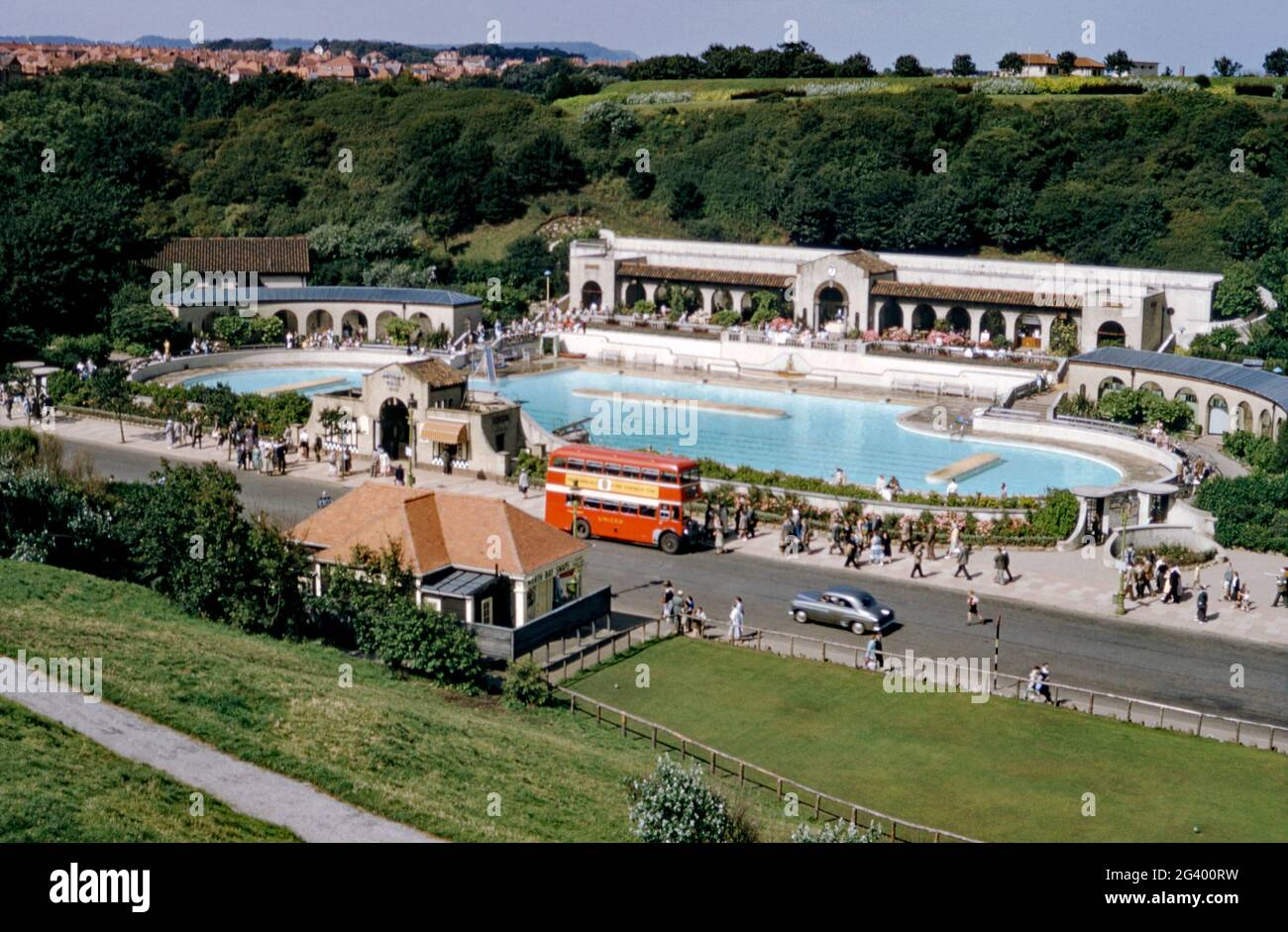 A view c. 1960 of the North Bay Bathing Pool, Peasholm Gap, Scarborough, East Yorkshire, England, UK was a popular attraction for swimmers at the seaside resort. The buildings are in a mediterranean style and a red ‘United’ bus is stopped outside. Previously a boating lake, it was remodelled in 1938, with accommodation for swimmers, sunbathers and seating for spectators. The North Bay Bathing Pool later became Waterscene, which boasting the longest water chute in the world in 1984. It closed in 2007 and was demolished to make way for apartments. This image is from an old vintage transparency. Stock Photo