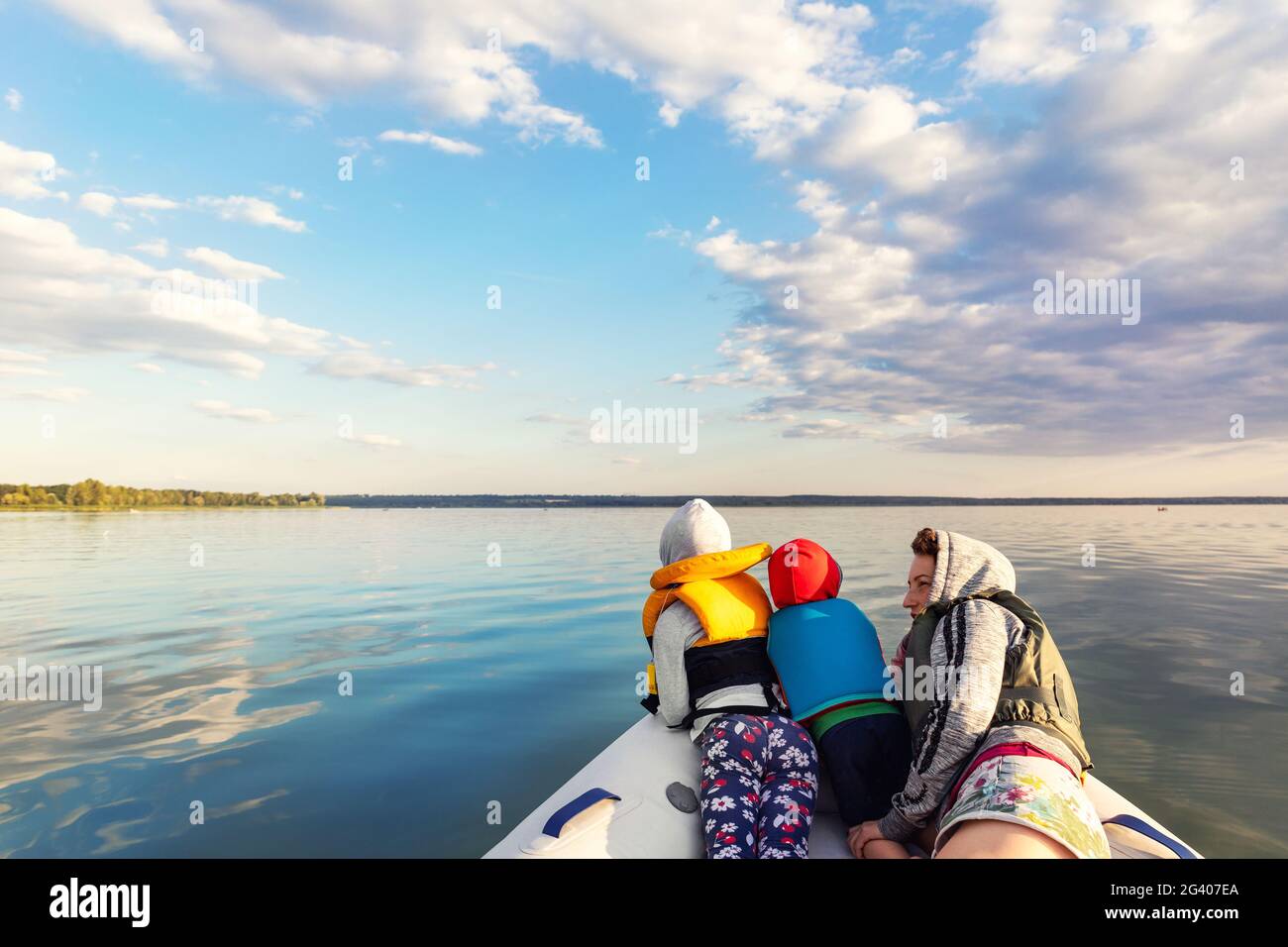 Bacl view two cute adorable little caucasian sibling together with mother wearing lifejacket vest having fun enjoy riding inflatable motorboat river Stock Photo